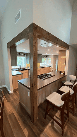 Modern kitchen with wooden beams, island, bar stools, and large windows for natural light.