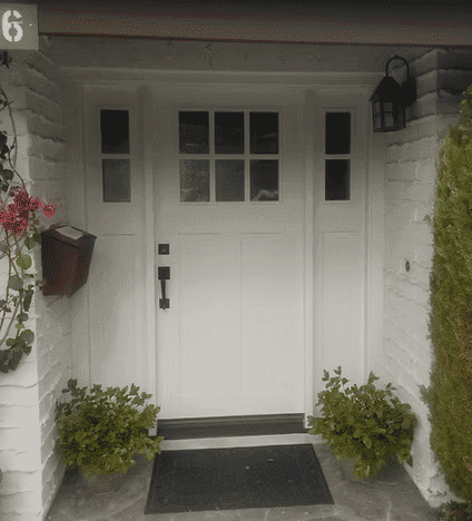 Elegant white front door with glass panels, surrounded by potted plants and brick wall.