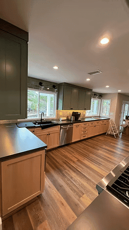 Modern kitchen with green cabinets, wood flooring, stainless steel appliances, and natural light.