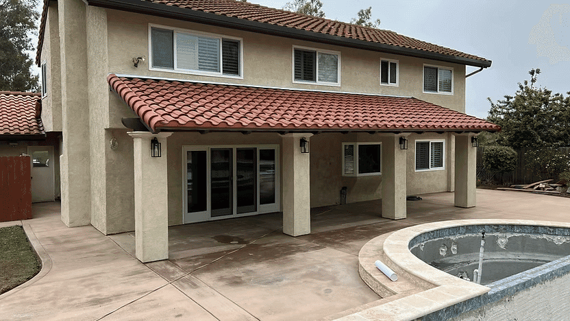 Two-story house with Spanish tile roof, patio, and empty pool in a suburban backyard.