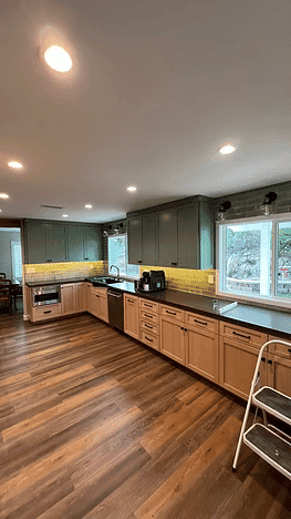 Modern kitchen with green cabinets, wooden flooring, and natural light from large windows.