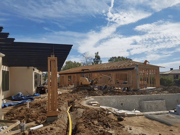 Construction site featuring a wooden frame house, equipment, and cloudy blue sky.