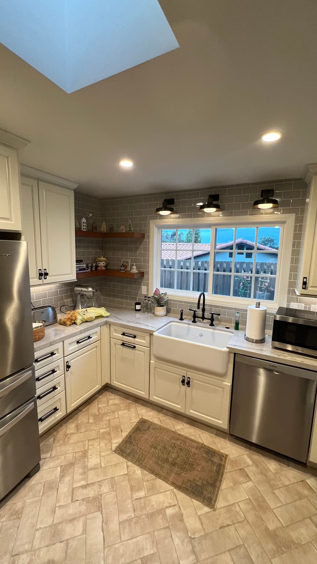 Modern kitchen with white cabinets, farmhouse sink, and skylight, featuring stylish gray tile accents.