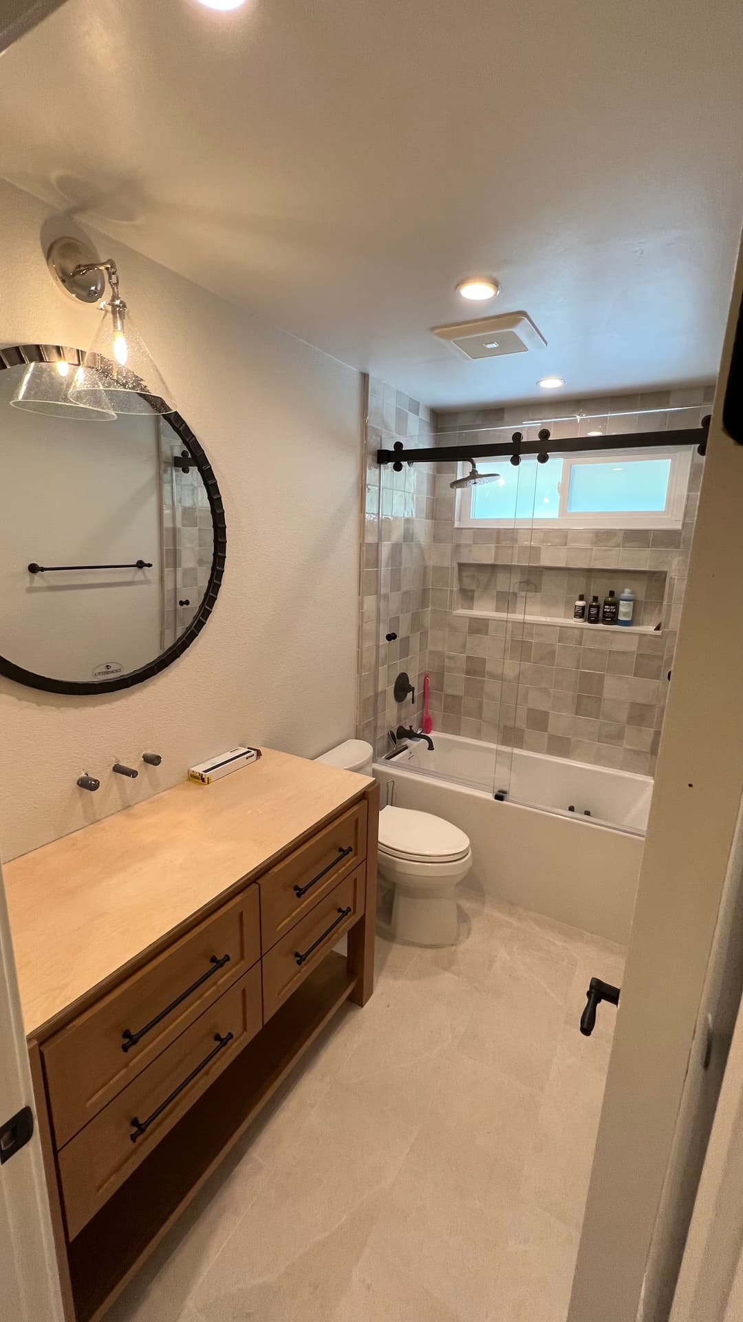Modern bathroom featuring a round mirror, wooden vanity, and elegant tile design.