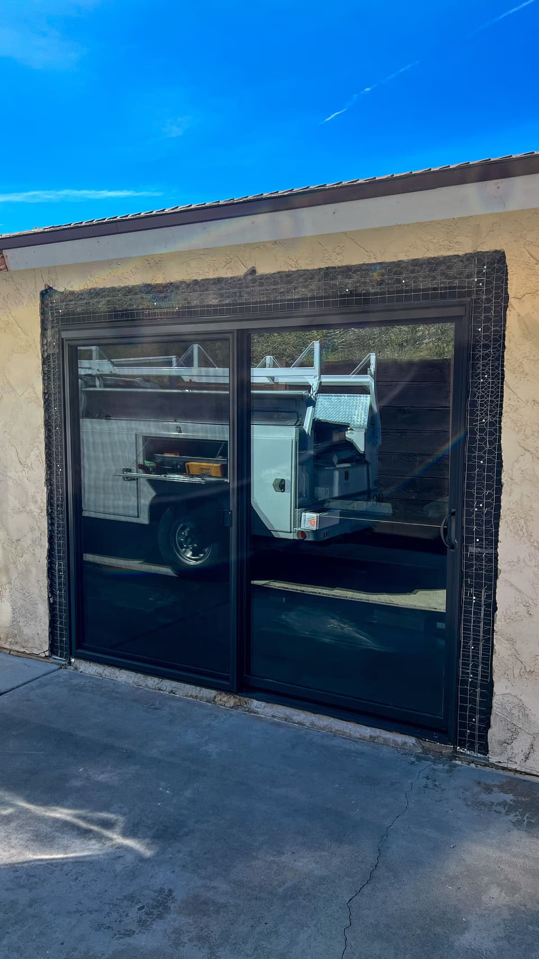 Sliding glass door with a black frame and textured wall, truck reflected in the glass.