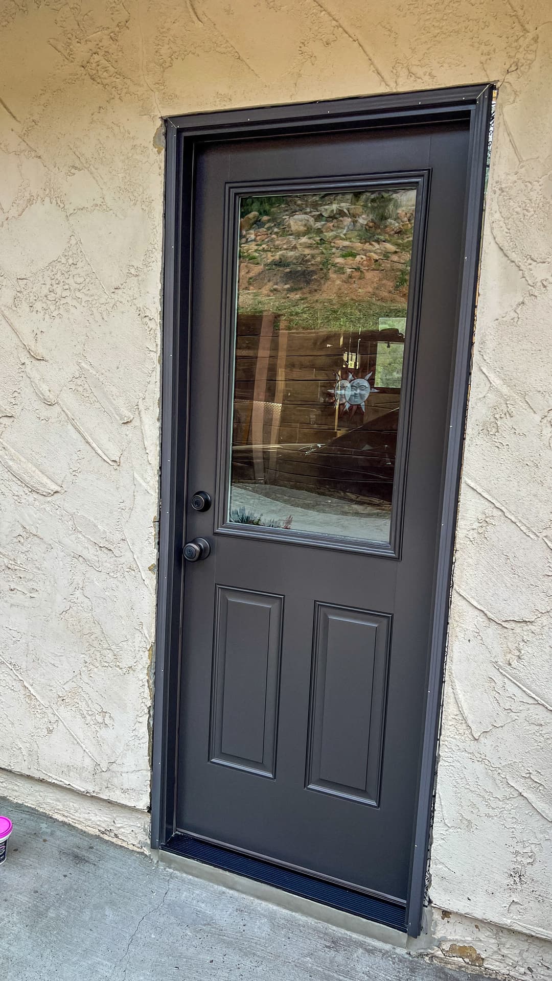 Black panel door with a glass window, set in a textured beige wall.