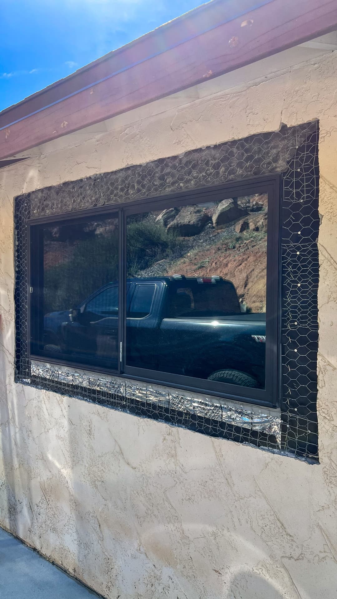 Modern window with black frame and decorative tile, reflecting a truck in the background.