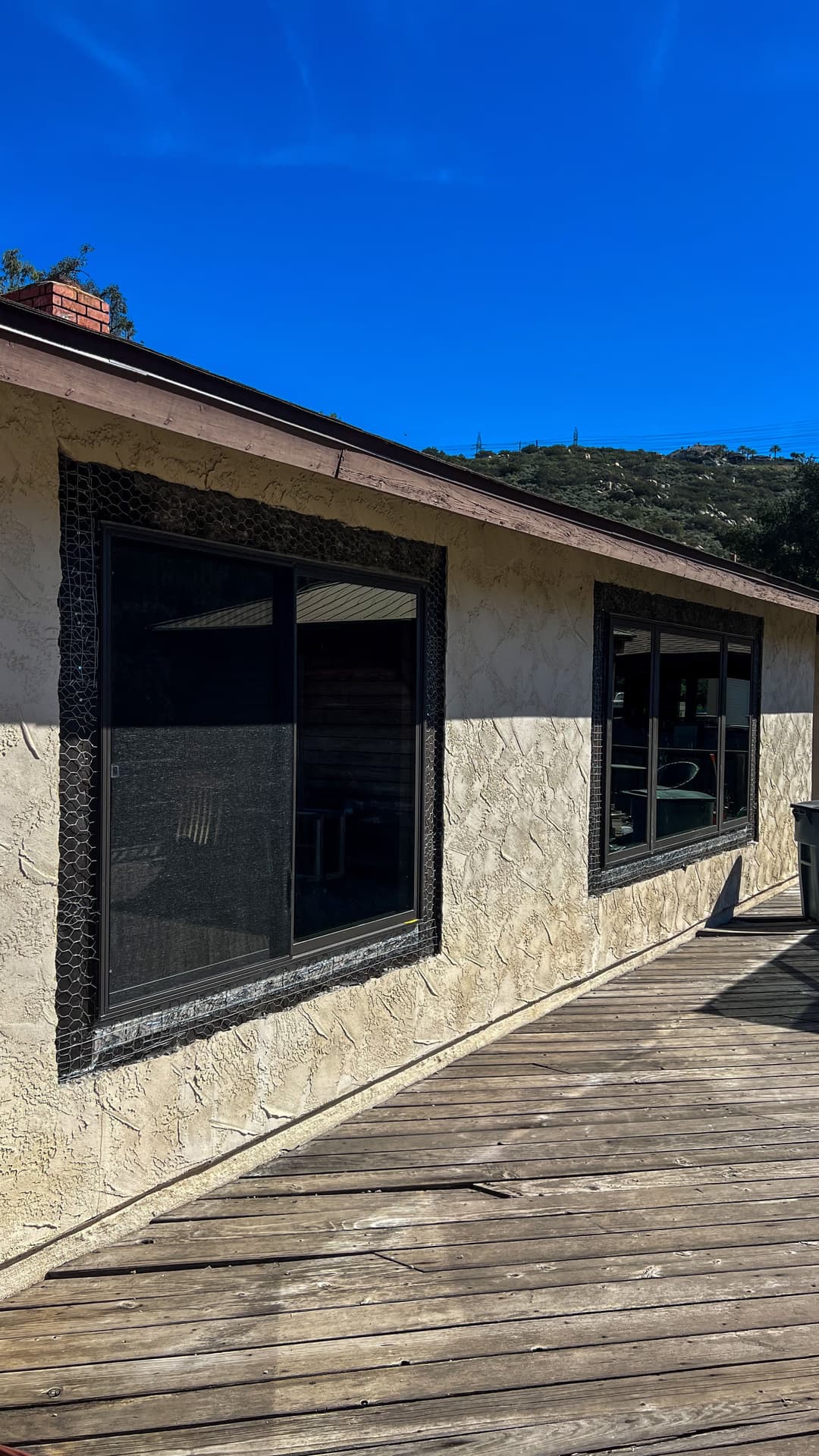 Exterior view of a house with textured walls, large windows, and a wooden deck under a blue sky.