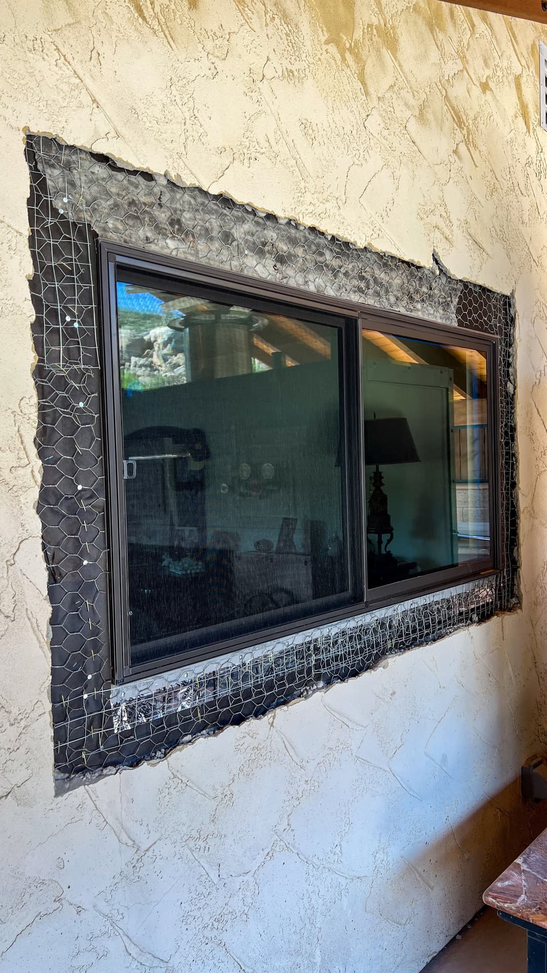 Window installation with wire mesh frame on textured beige wall, showcasing renovation details.