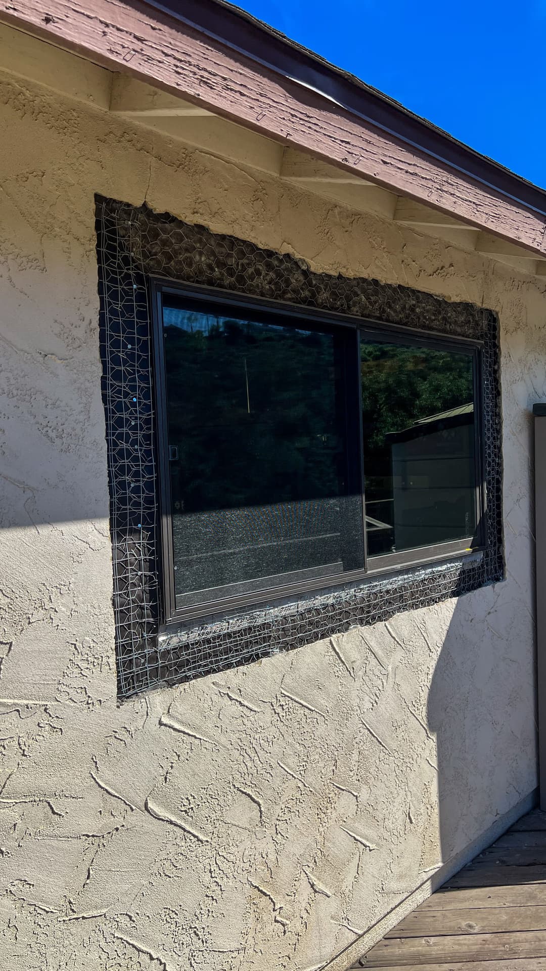 Modern window with decorative wire mesh trim on textured stucco wall, under a clear blue sky.