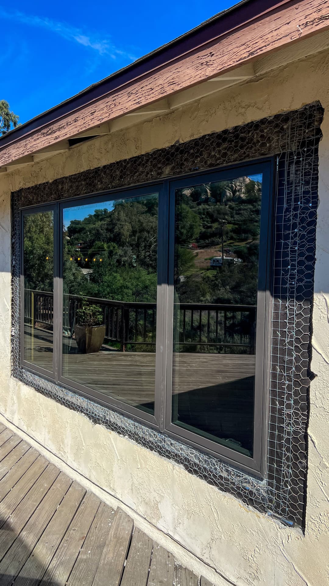 Modern home window with textured frame, overlooking a scenic deck and landscape.