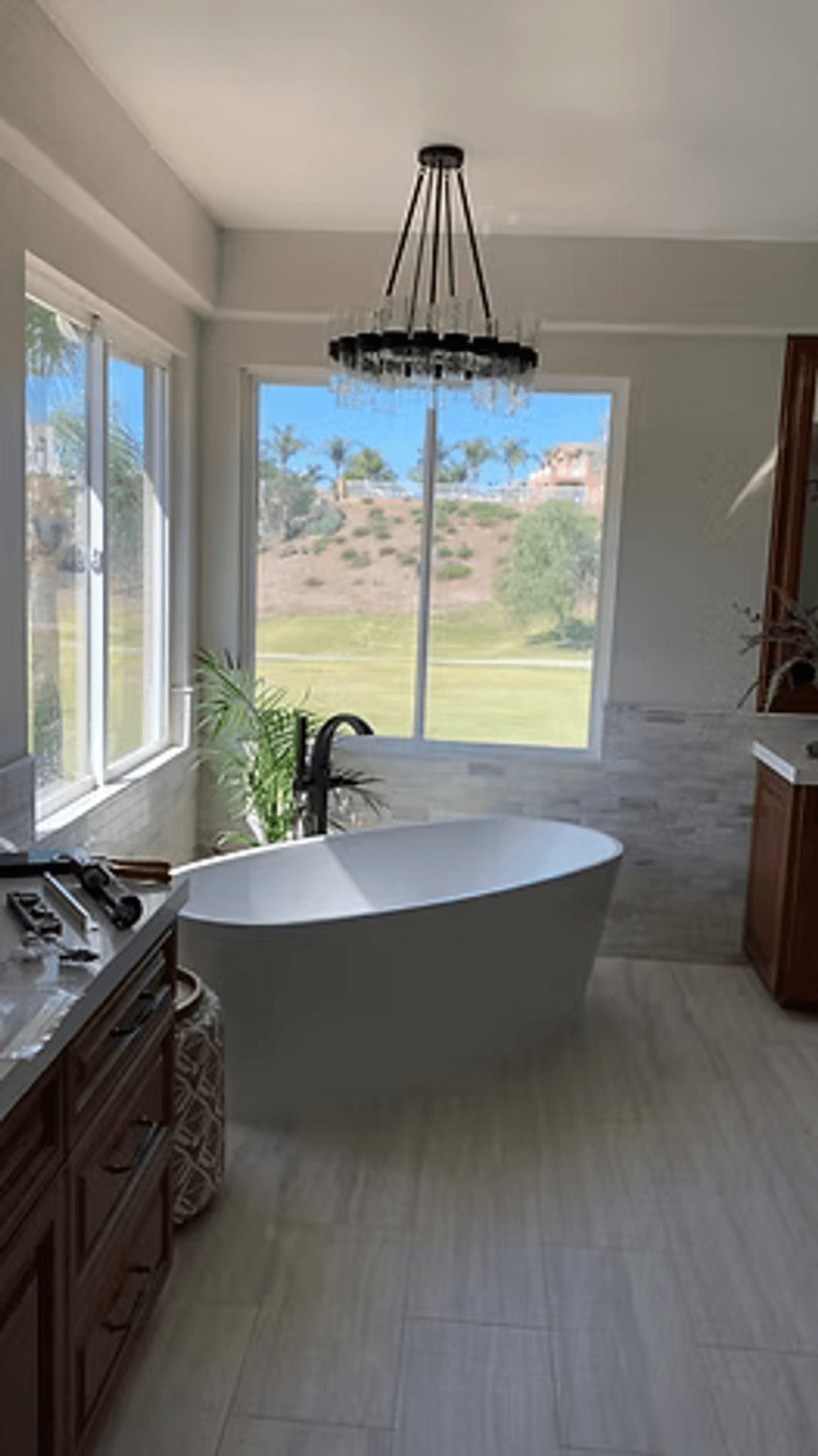 Modern bathroom with a freestanding tub, large window, and stylish fixtures overlooking greenery.