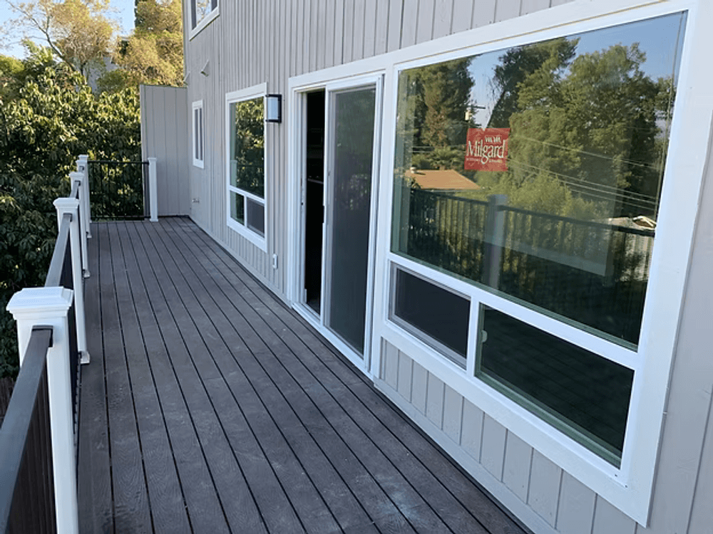 Spacious wooden deck with large windows and a scenic view of greenery.